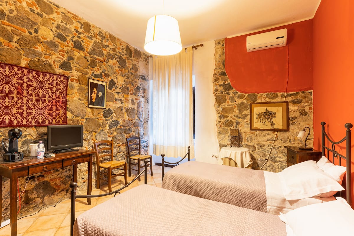A room with two beds, a desk with a computer, a chair, and a stone wall.
