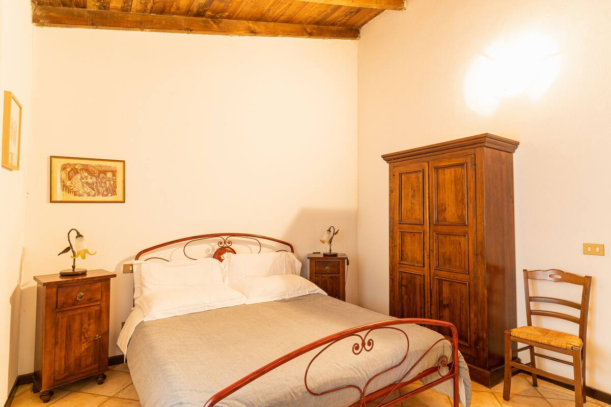 A bedroom with a single bed, wooden nightstands, a wooden wardrobe, a chair, and a wall-mounted light fixture.