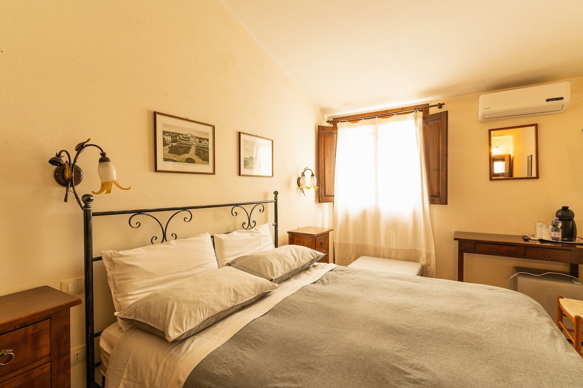 A bedroom with a bed, bedside tables, a desk with a chair, an air conditioner, and a window with curtains.