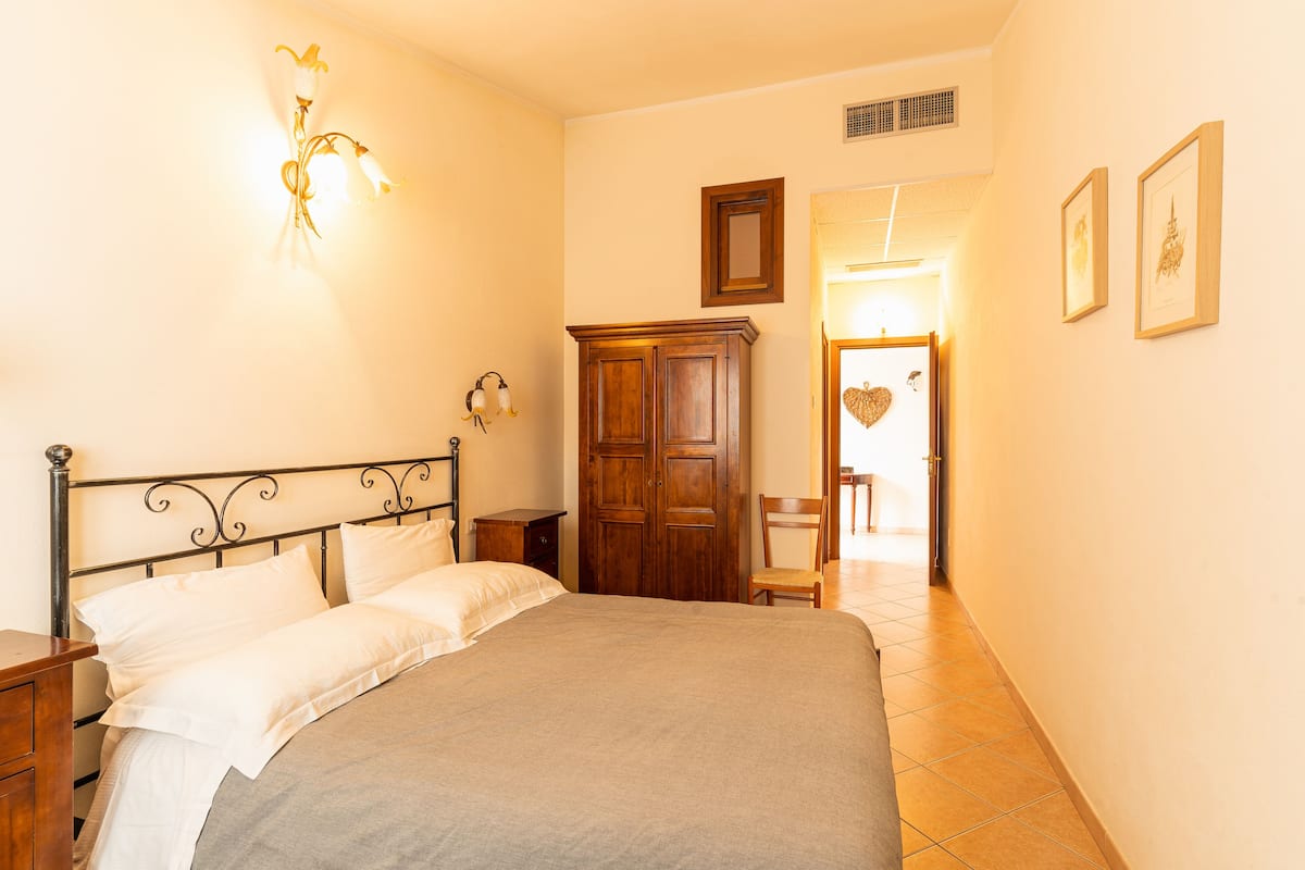 A bedroom with a bed, wooden wardrobe, and a wall-mounted light fixture.