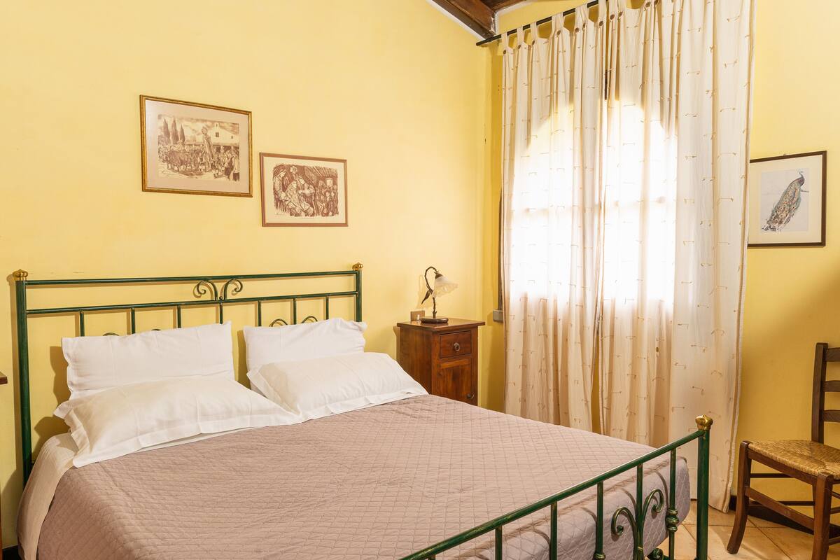 A bedroom with a bed, a nightstand, a chair, and two framed pictures on the wall.