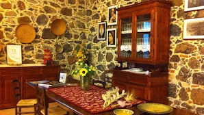 Une pièce aux murs de pierre, avec une table à manger en bois, des chaises et un buffet aux portes vitrées.