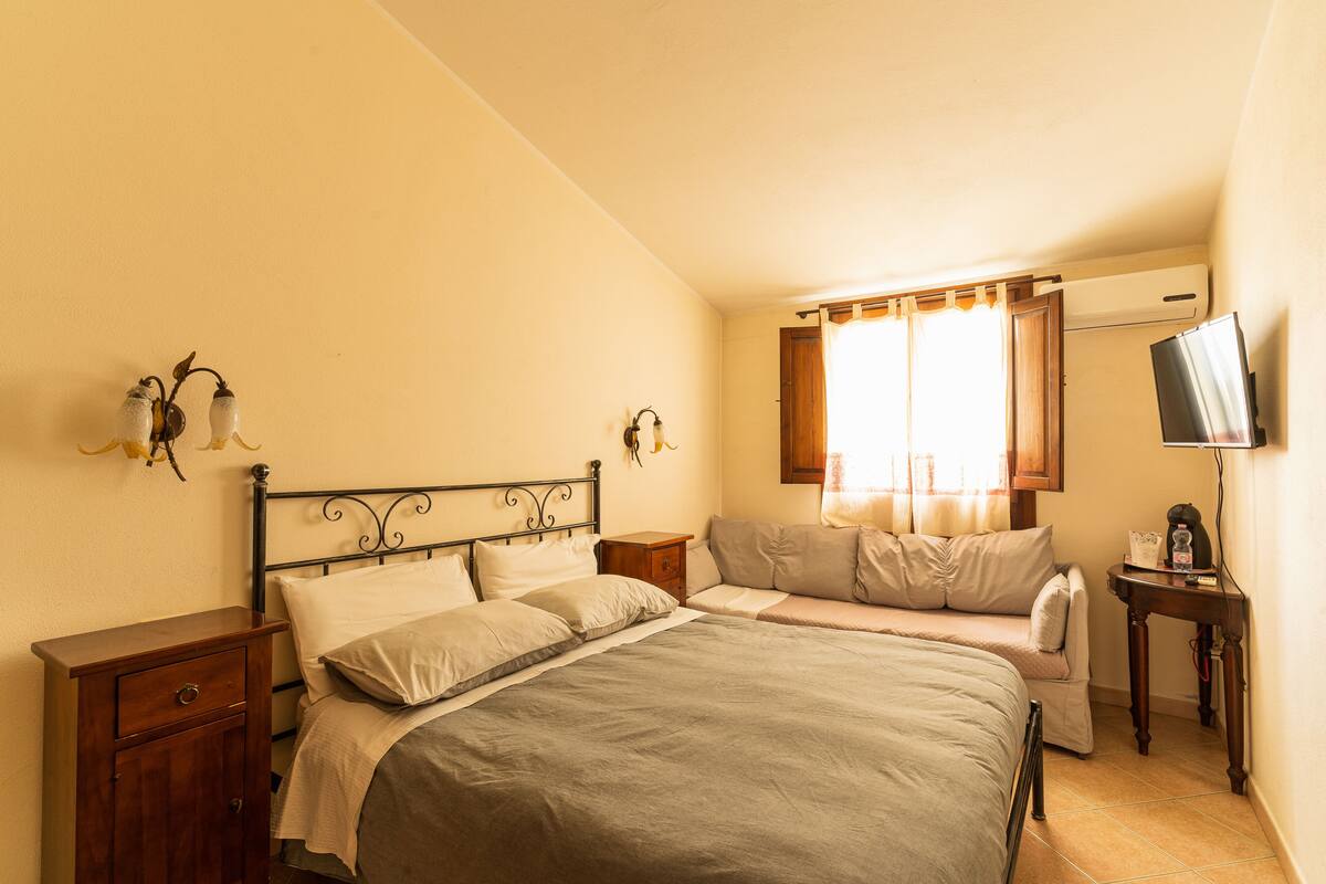 A bedroom with a bed, bedside tables, a TV, and a window with curtains.