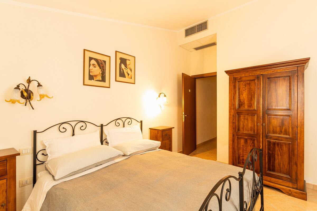 A bedroom with a bed, nightstands, a wardrobe, and wall-mounted lights.