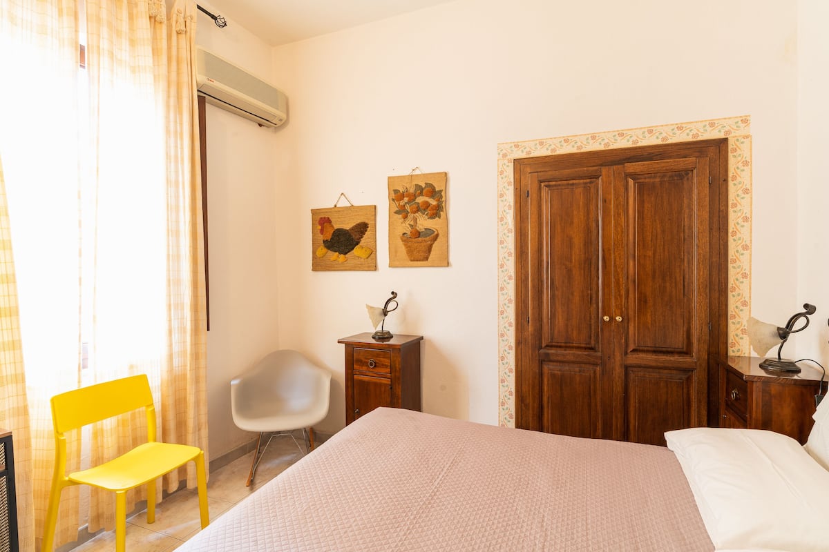 A bedroom with a bed, a chair, a wooden wardrobe, and two wall-mounted pictures.