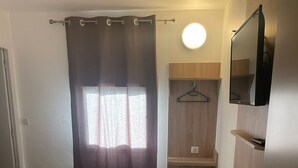 A bedroom with a bed, a window with curtains, a TV, and a wooden shelf. - My KB Hotel Montélimar (Saulce-sur-Rhone)