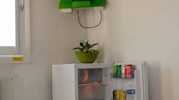 Una habitación con una cama, un televisor montado sobre un soporte verde, un refrigerador y una ventana.