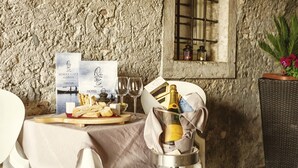 Ein Tisch ist gedeckt mit einer Champagnerflasche, Gläsern, einer Speisekarte und einem Teller Essen in rustikalem Ambiente mit Steinwänden und einem Fenster.