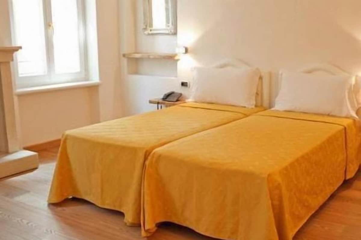 Una cama doble con una colcha amarilla en una habitación con suelo de madera y una ventana.