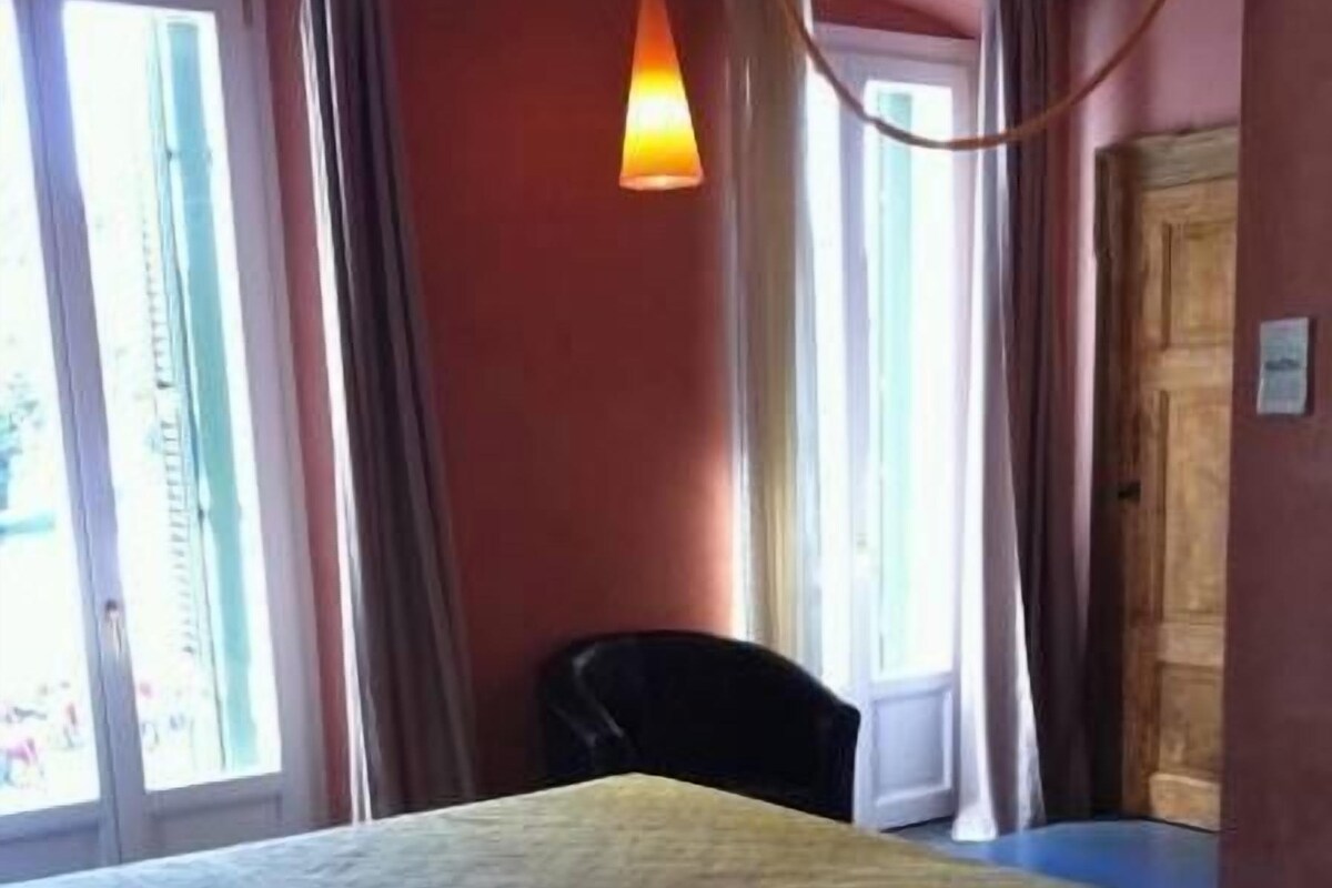 Una habitación con una cama, una silla y un ventanal con cortinas.