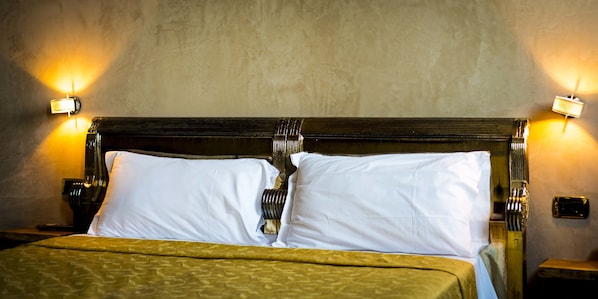 Una cama con cabecera, dos lámparas de noche y una lámpara fijada a la pared.
