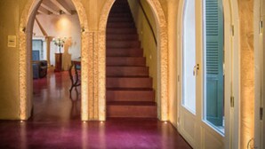 Ein Flur mit einer Holztreppe, bogenförmigen Durchgängen und einem großen Fenster.