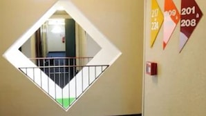 Un couloir d’hôtel avec un motif géométrique sur le mur, un panneau indiquant la sortie de secours et des panneaux de signalisation numérotés.
