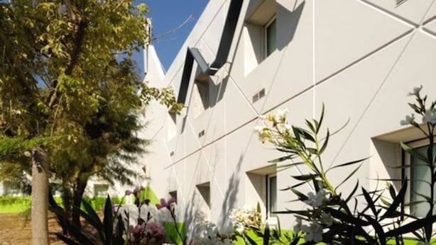 Un bâtiment moderne à l’architecture géométrique, entouré de verdure et de plantes en fleurs.