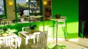 Un coin repas avec des chaises et des tables blanches, un mur d’accent vert et une plante en pot ornée de fleurs blanches.