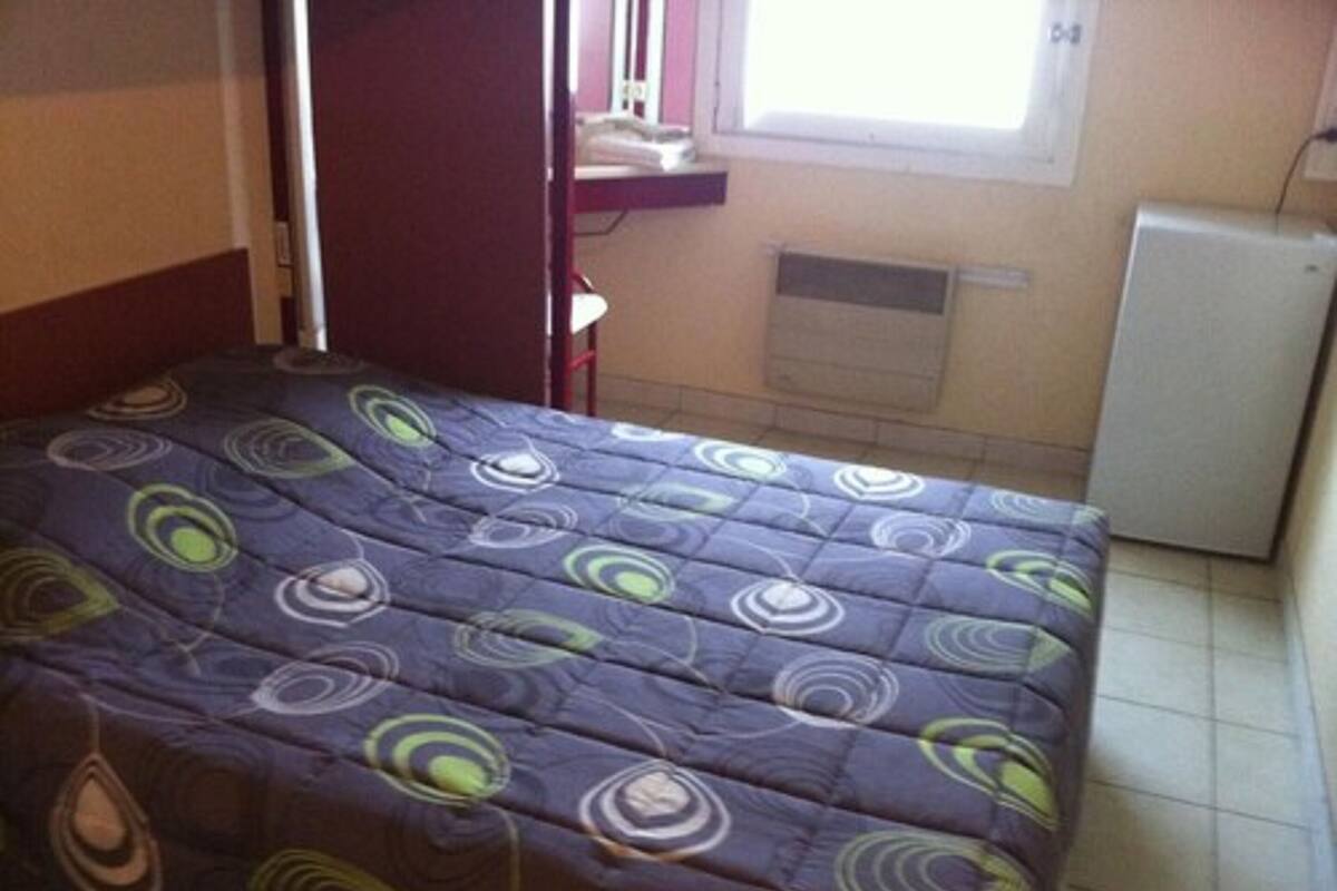 A bedroom with a bed, a window, a radiator, and a small white appliance.