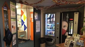 Un petit hall d’hôtel, à l’aménagement compact, comprenant un distributeur automatique, une poubelle et un comptoir de réception où sont disponibles des brochures d’information.