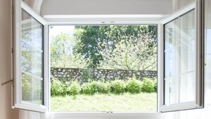 Ein Schlafzimmer mit offenem Fenster, einem Heizkörper und einem Bett mit Blumendekoration.