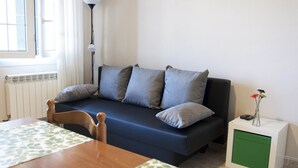 Ein modernes Wohnzimmer mit einem dunkelblauen Sofa, einem Holzessttisch und einer kleinen, grünen Kommode.