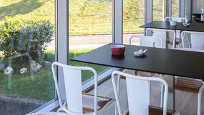 Ein moderner Essbereich mit großem Tisch und weißen Stühlen, große Fenster mit Blick auf eine grüne Landschaft.