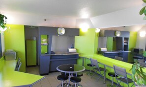 A brightly colored cafe with a round table and chairs, a counter with a cash register, and a clock on the wall. - Lemon Hotel Le Coteau Roanne (Le Coteau)