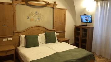 Ein Zimmer mit einem hölzernen Bett, grünen Kissen, einem Fernseher auf einer Holzkommode und einer wandmontierten Lampe.