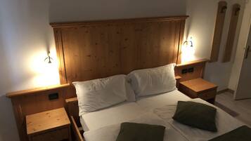 A wooden-framed bed with white linens and two green pillows, flanked by wooden nightstands with wall-mounted lamps.