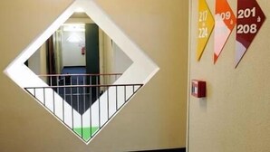 Un pasillo de hotel con un muro espejado, señal de salida de emergencia y carteles direccionales numerados.