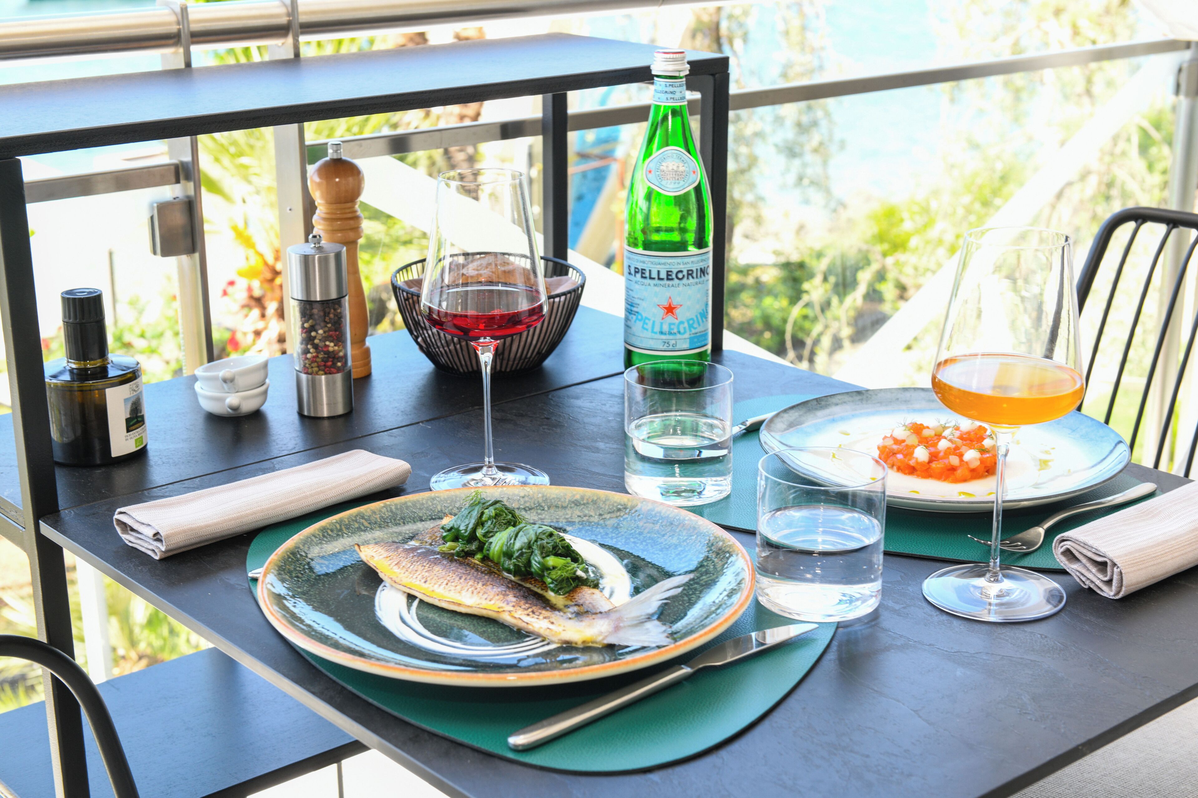 Una mesa con comida, una botella de agua Pellegrino, una copa de vino tinto y un vaso de jugo de naranja.