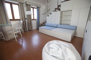 Ein modernes Wohnzimmer mit einer Couch, einem Esstisch, Stühlen, einer Treppe und eingebauten Regalen.