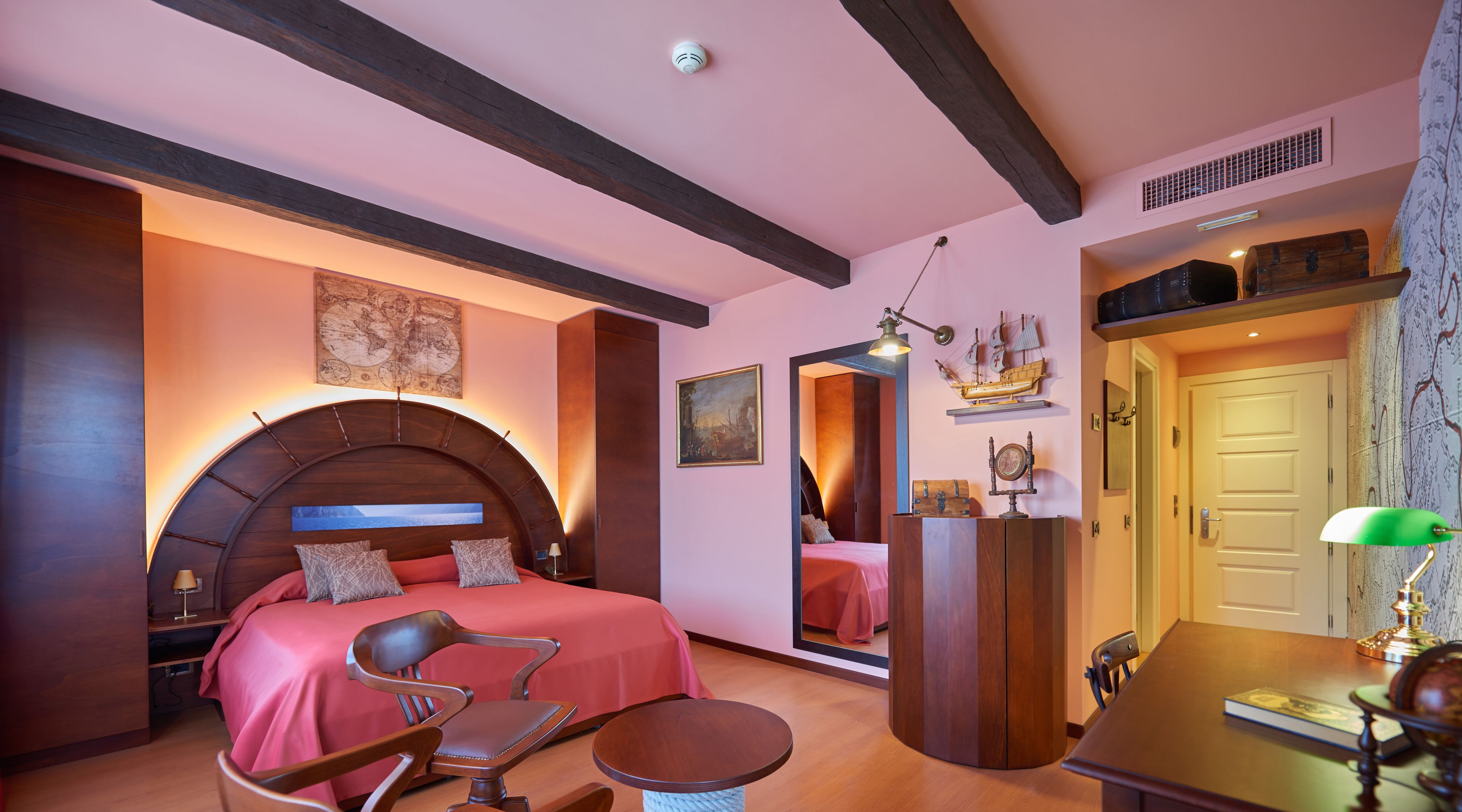 A bedroom with a large bed, a wooden headboard, a desk with a lamp, and a mirror.
