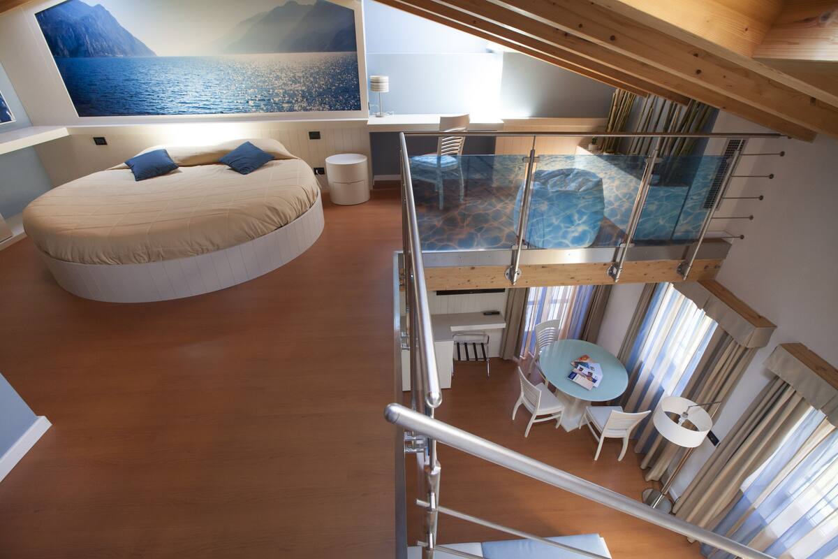 Un dormitorio moderno con una cama redonda, un balcón de cristal y una zona de comedor con mesa y sillas.