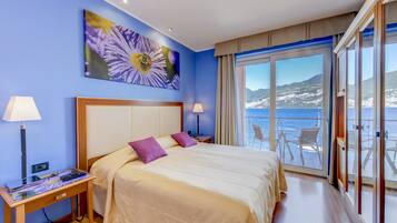 Quarto de hotel com uma cama, duas mesas de cabeceira, um quadro de uma flor e uma varanda vista para o mar.
