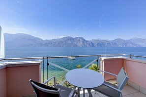 A balcony with a table and chairs overlooking a body of water and mountains. - Belfiore Park Hotel - Adults Only  (Brenzone sul Garda)