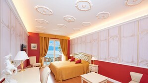 Een hotelkamer met een groot bed, een bureau, een stoel en uitzicht op zee.