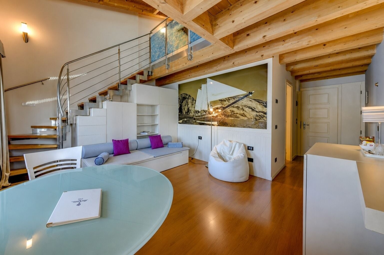 Ein modernes Interieur mit einer Treppe, einem Glastisch, einem Sitzsack und einem großen Gemälde.