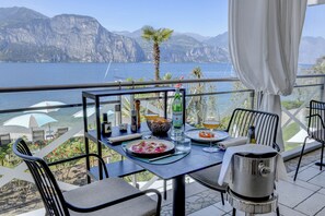 A balcony with a table set for dining, overlooking a body of water and mountains.