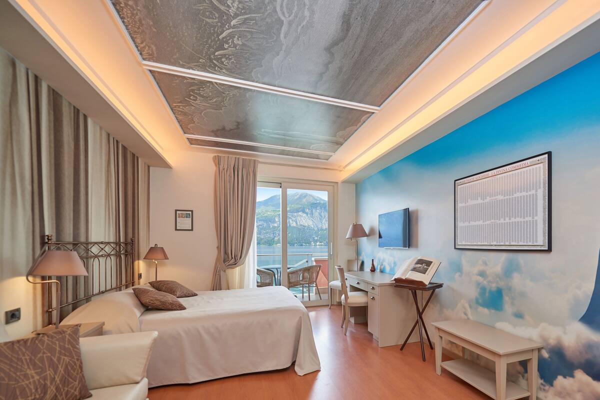 Habitación de hotel con dos camas, un escritorio, una silla, un televisor y un mural con la imagen de dos figuras en la pared.