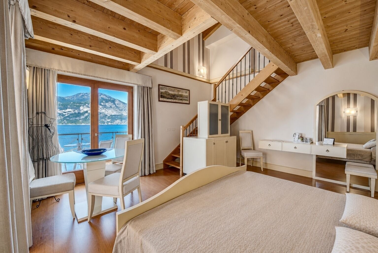 Ein Schlafzimmer mit Bett, Schreibtisch, Stuhl, einer Treppe und Blick auf das Meer.