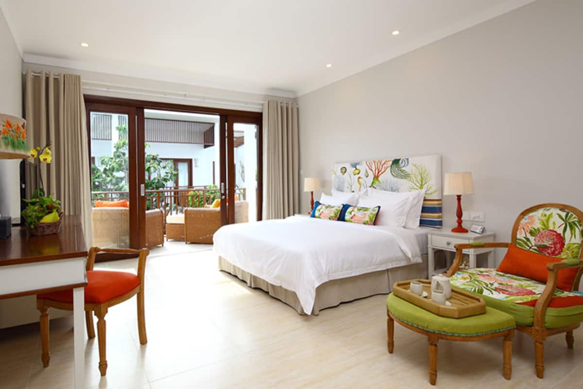 A hotel room with a bed, desk, chair, and a balcony with outdoor furniture.