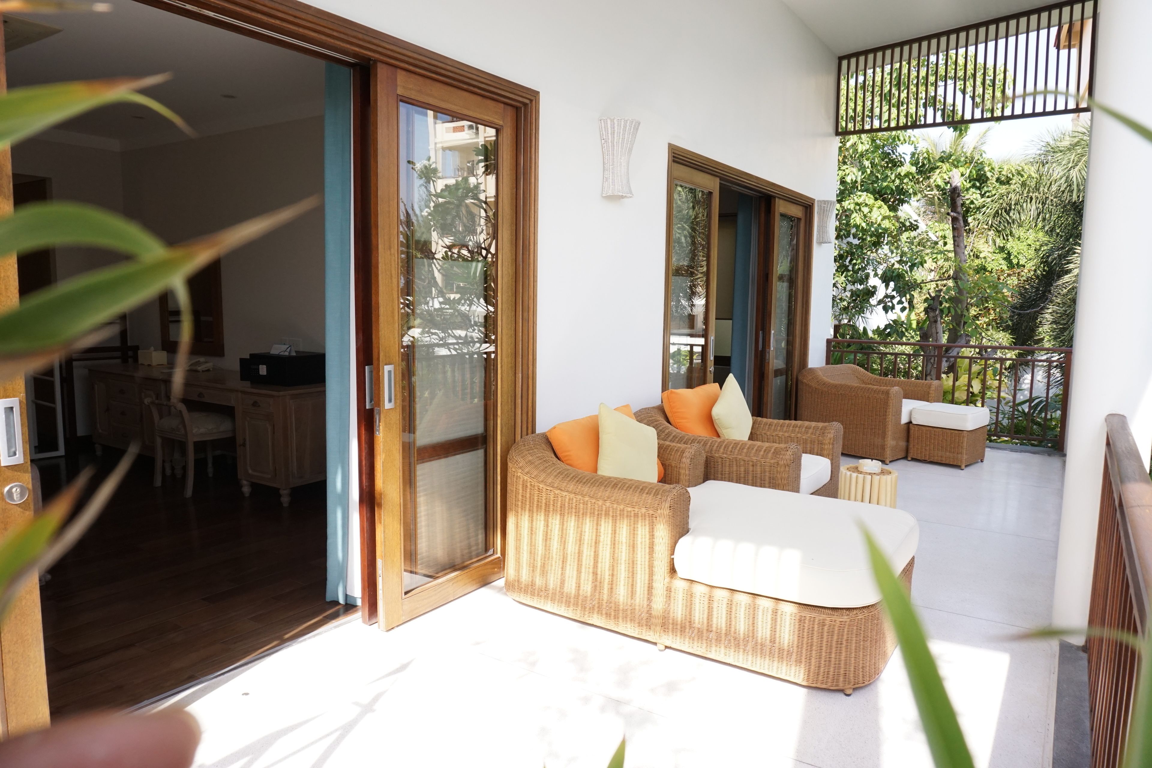 Un salón moderno con muebles de mimbre, un ventanal de vidrio que da a un balcón y un comedor visible a través del ventanal.