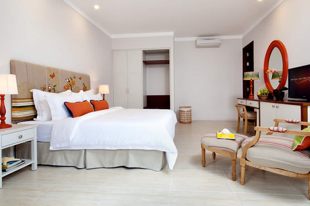 A hotel room with a bed, bedside tables, a desk with a chair, a television, and a wardrobe.