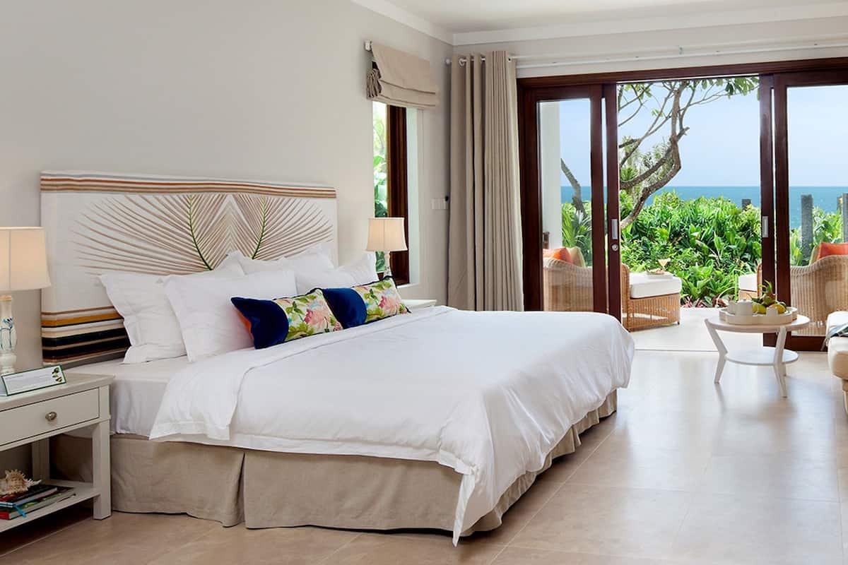 A spacious hotel room with a large bed, a sitting area with a view of the ocean, and a dining table.