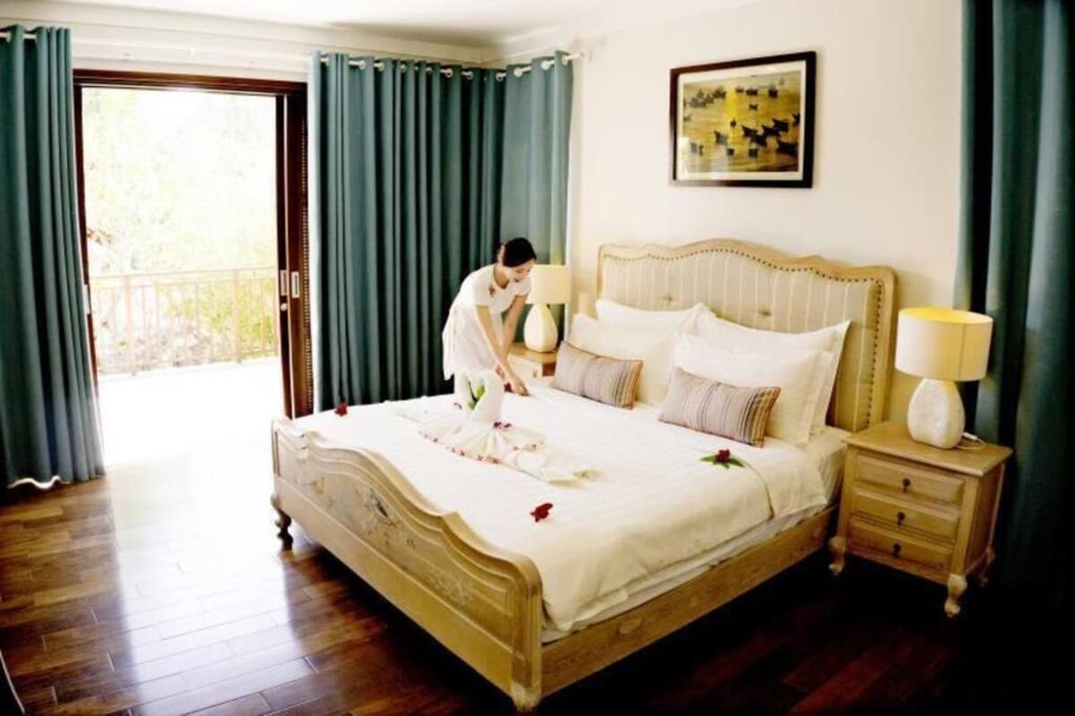 A neatly made bed with a headboard, a bedside table with a lamp, and a painting on the wall.