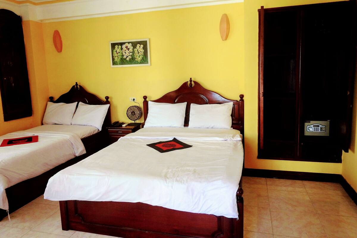 A hotel room with two single beds, a bedside table with a phone, a wall-mounted clock, and a door with a security keypad.