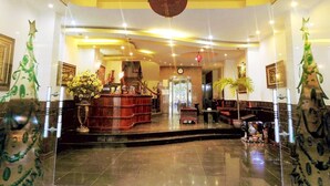 A lobby with a reception desk, a clock, and a staircase leading to an elevator. - La Suisse Hotel (Nha Trang)