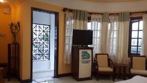 A hotel room with a bed, a TV on a cabinet, two chairs, a small table, and a door with a view of the outside. - La Suisse Hotel (Nha Trang)