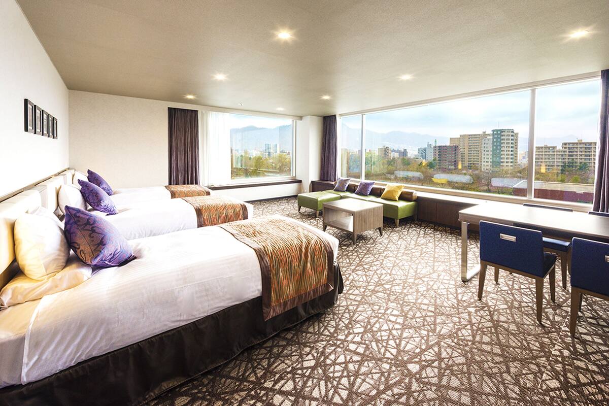 A hotel room with two beds, a desk, and a view of the city.