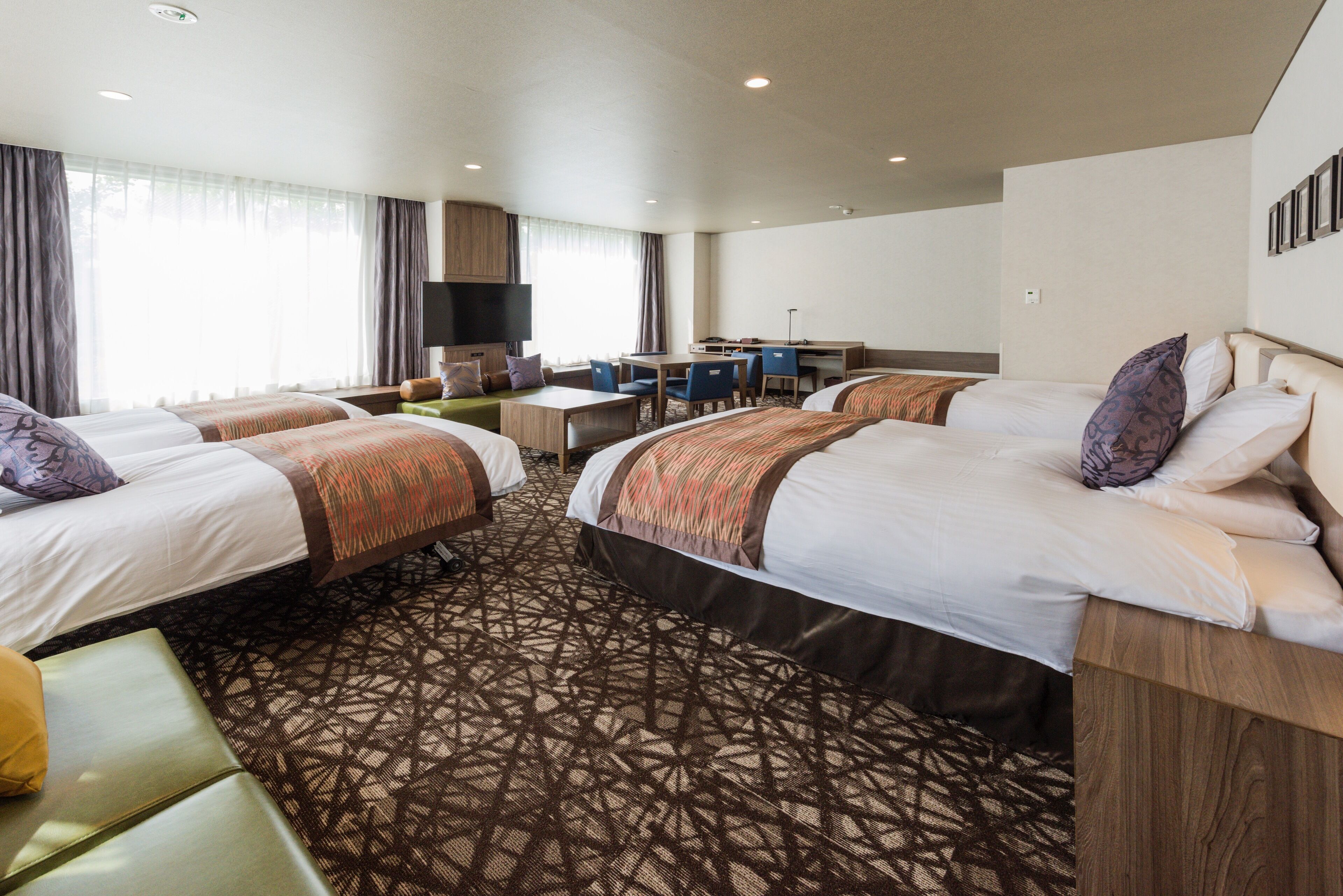 A hotel room with two beds, a desk, a chair, and a TV.