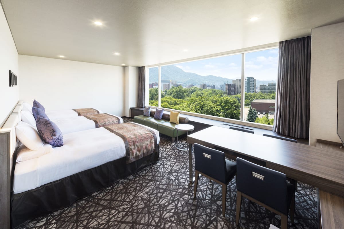 A hotel room with a bed, a sofa, a desk, and a view of a cityscape.